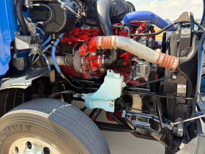 Peterbilt truck engine bay with red engine and blue hoses, large intake hose, coolant reservoir, and various metallic components visible.
