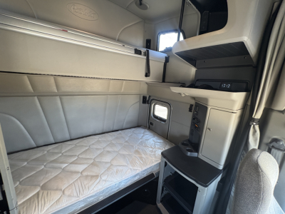 Peterbilt 579 sleeper cab interior with upper bunk, left side storage, quilted mattress, control panels and a small window.