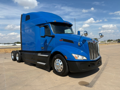 Peterbilt 579 truck with blue cab and sleeper, front view at slight angle, chrome wheels, black bumper, two exhaust stacks, side mirrors, clear sky.