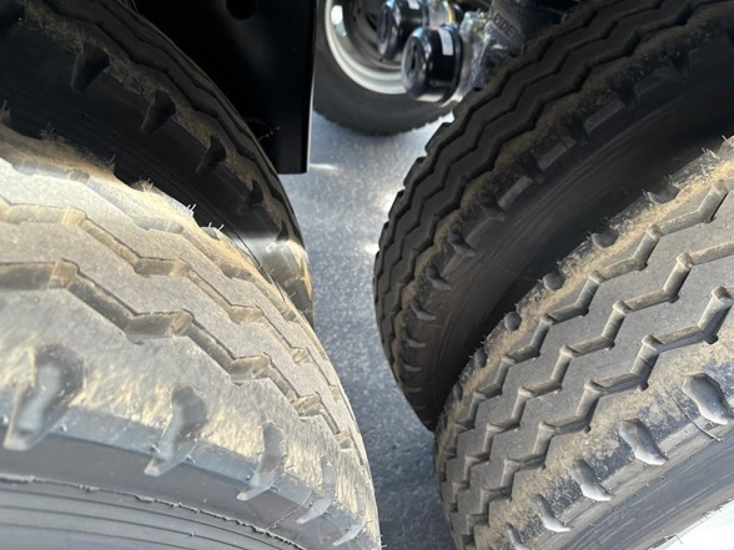 Two large truck tires viewed from between the rear wheels of a Manac Combo Drop Deck trailer.