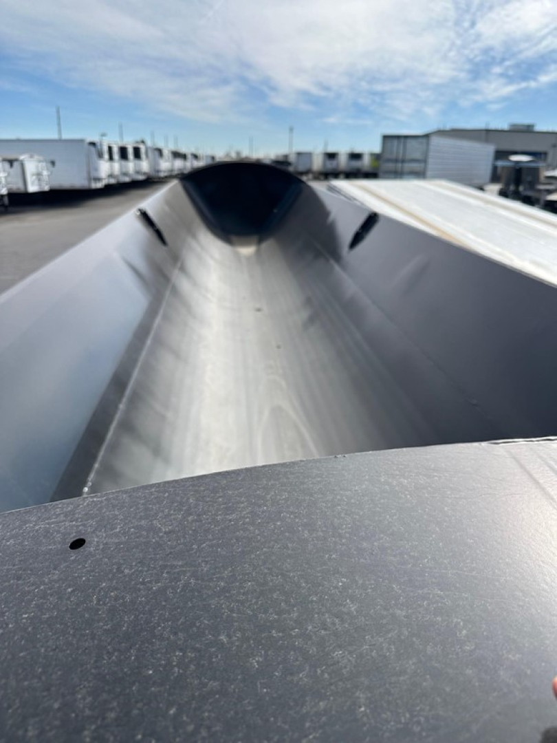 Inside view of a Manac combo drop deck trailer trough/bed showing a smooth metal surface and side rails, with distant trailers and buildings in the background.