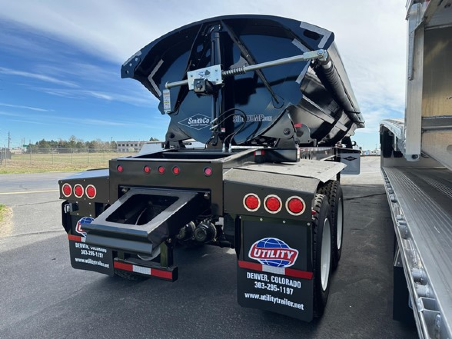 Manac combo drop deck trailer viewed from rear showing hydraulic staging and rear bumper with taillights; Utility logo mud flaps and deck mechanism visible.