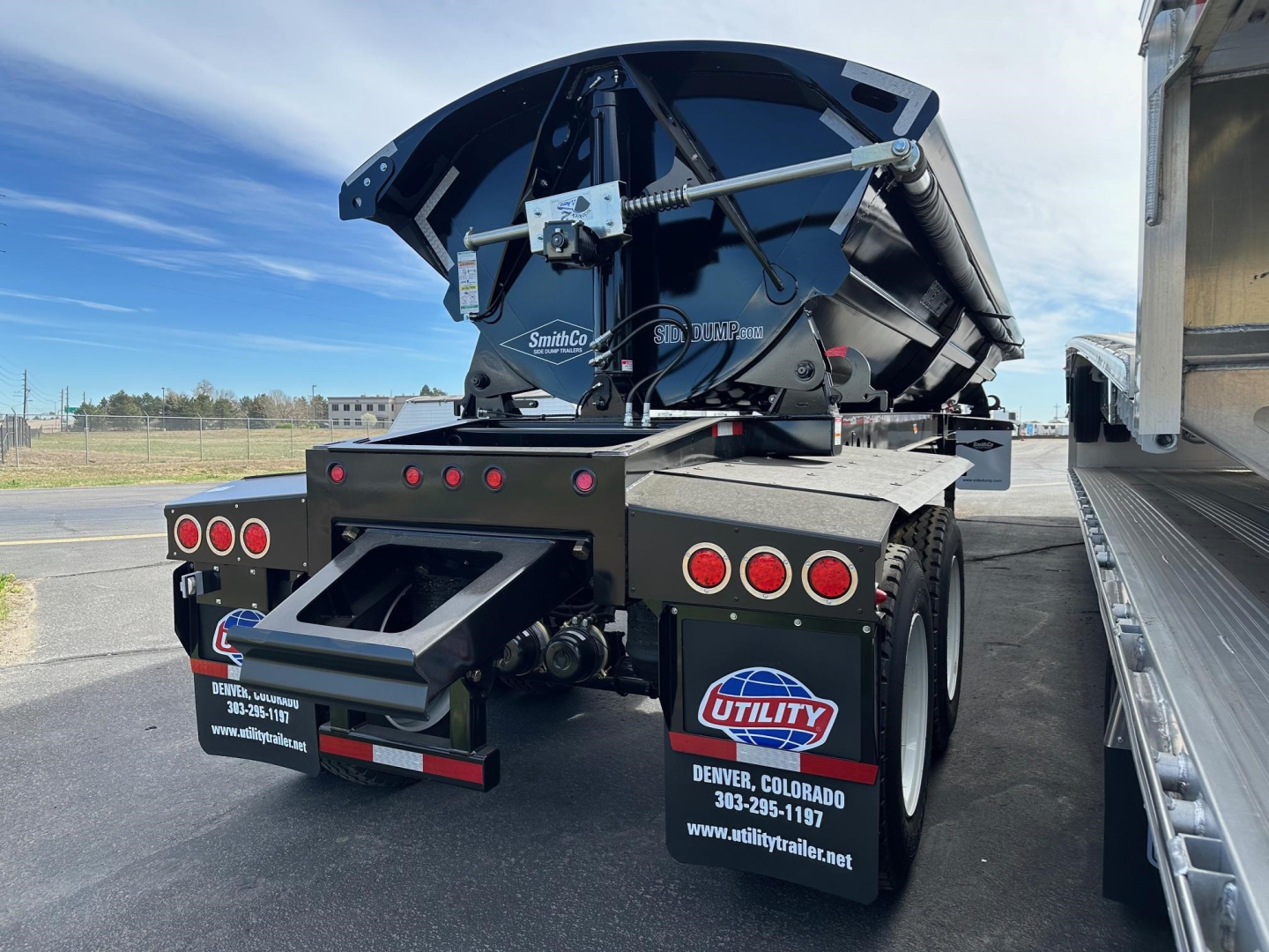Manac combo drop deck trailer rear view showing hydraulic dump body and mud flaps with utility logo