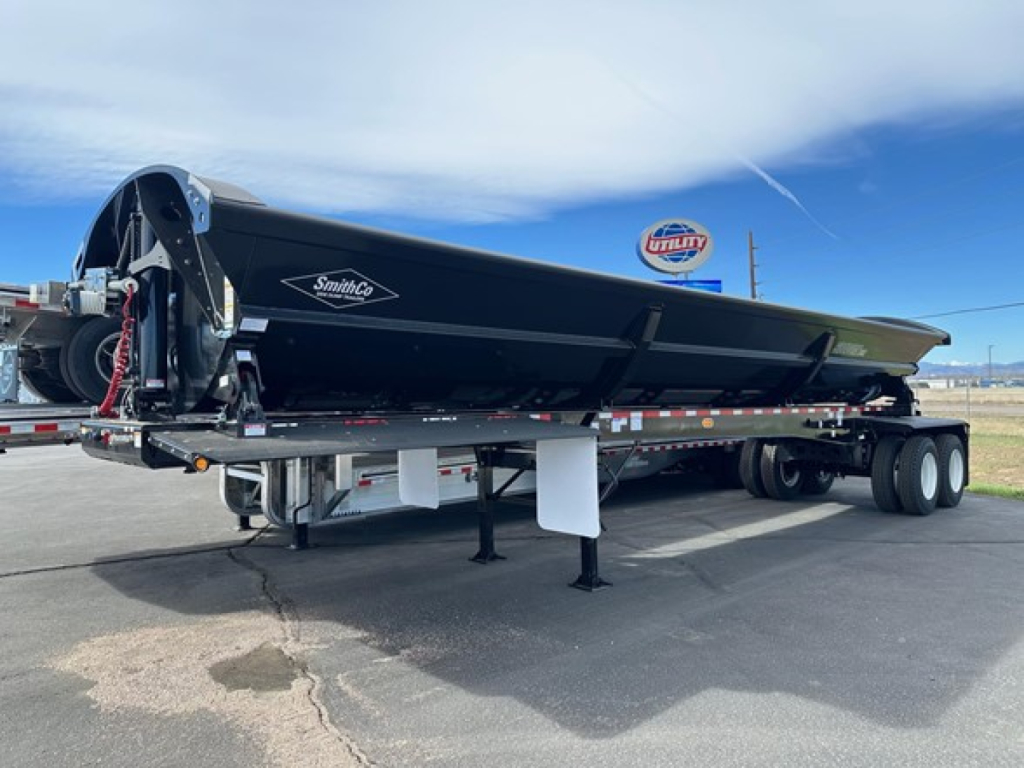 Manac combo drop deck trailer on a sunny day showing black bed with SmithCo logo and hydraulic system, trailer legs extended.