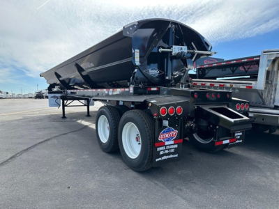Manac combo drop deck trailer with spread dual rear axles and black hopper bed, viewed from rear-side showing wheels, taillights, and hitch.