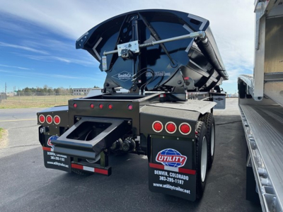 Rear of a Manac combo drop deck trailer with a blue and black storage unit mounted on upper frame. Visible text on mudflaps/readouts: Utility Denver Colorado and contact info. Tail lights and step plate visible.