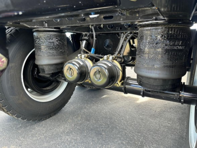 Under-car view of a 2026 Manac Combo Drop Deck trailer showing air suspension bags, axle, and brake components with hoses and fittings.