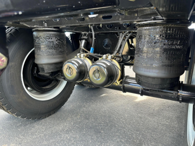 Manac combo drop deck trailer underside showing air tanks and hoses with labels in black paint; visible components include dual pneumatic tanks and axle area.