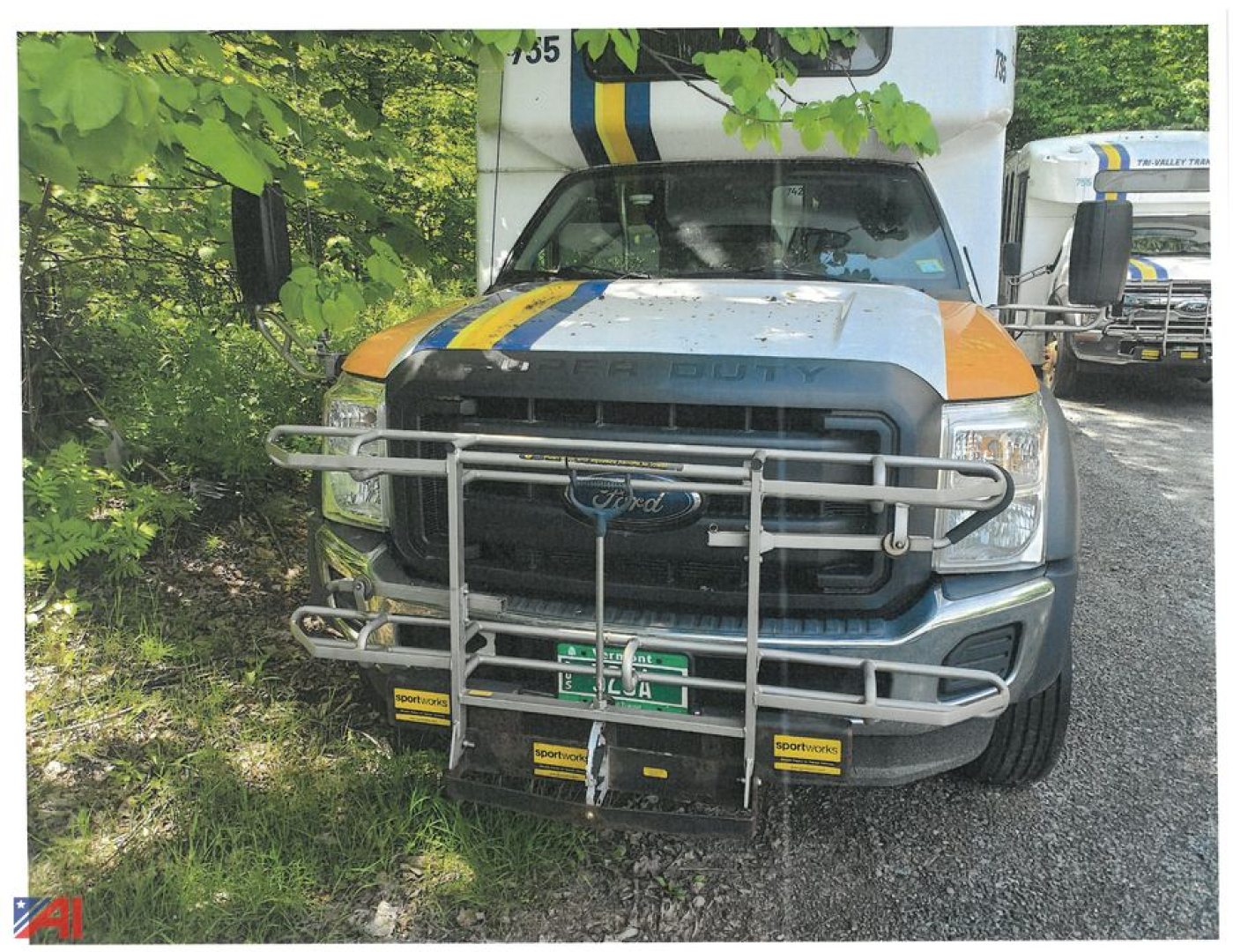 Ford F-550 Super Duty bus front view with grille guard and blue/yellow racing stripe, headlights visible.