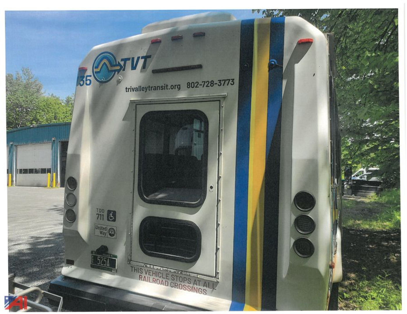 Ford F-550 Super Duty Bus rear view showing TRIVYLE TRANSIT logo and safety decals, rear window, vertical blue and yellow stripes on right side, rear bumper with warning text.