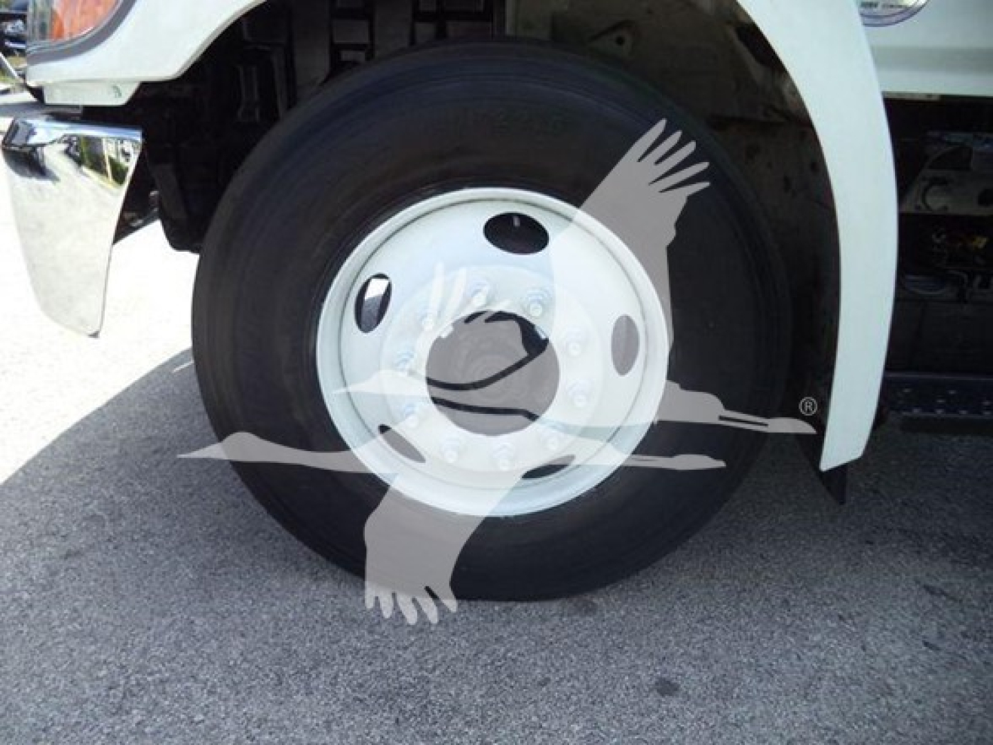 Front wheel of a Hino 268A dump truck showing steel wheel and tire, front fender, and part of the chassis.