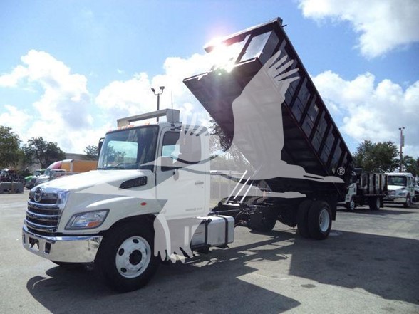 Dump truck in service showing white 2016 Hino 268A with raised dump bed in a dealership yard.