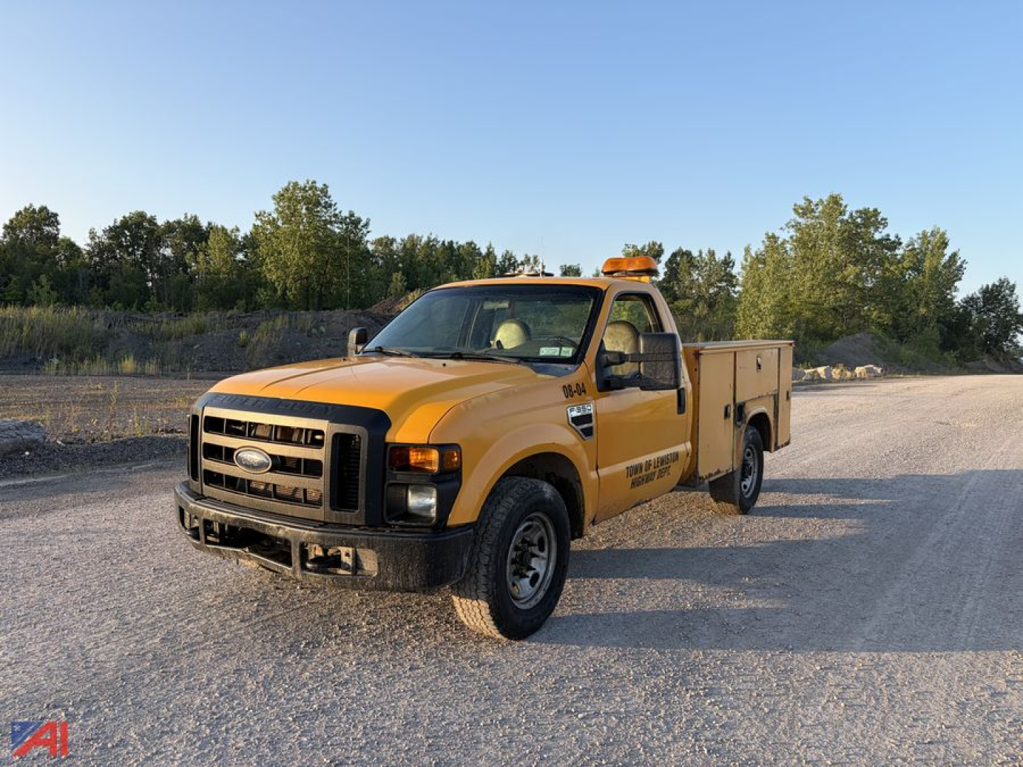 Ford F-350 Super Duty utility truck in a gravel lot, yellow service body, amber emergency beacon on cab roof, black front bumper, utility compartments along sides.