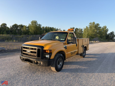 Ford F-350 Super Duty utility truck in a gravel lot, yellow service body, amber emergency beacon on cab roof, black front bumper, utility compartments along sides.