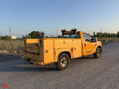 Ford F-350 Super Duty utility truck in service yellow with utility bed and amber warning light on cab roof, rear cargo area doors