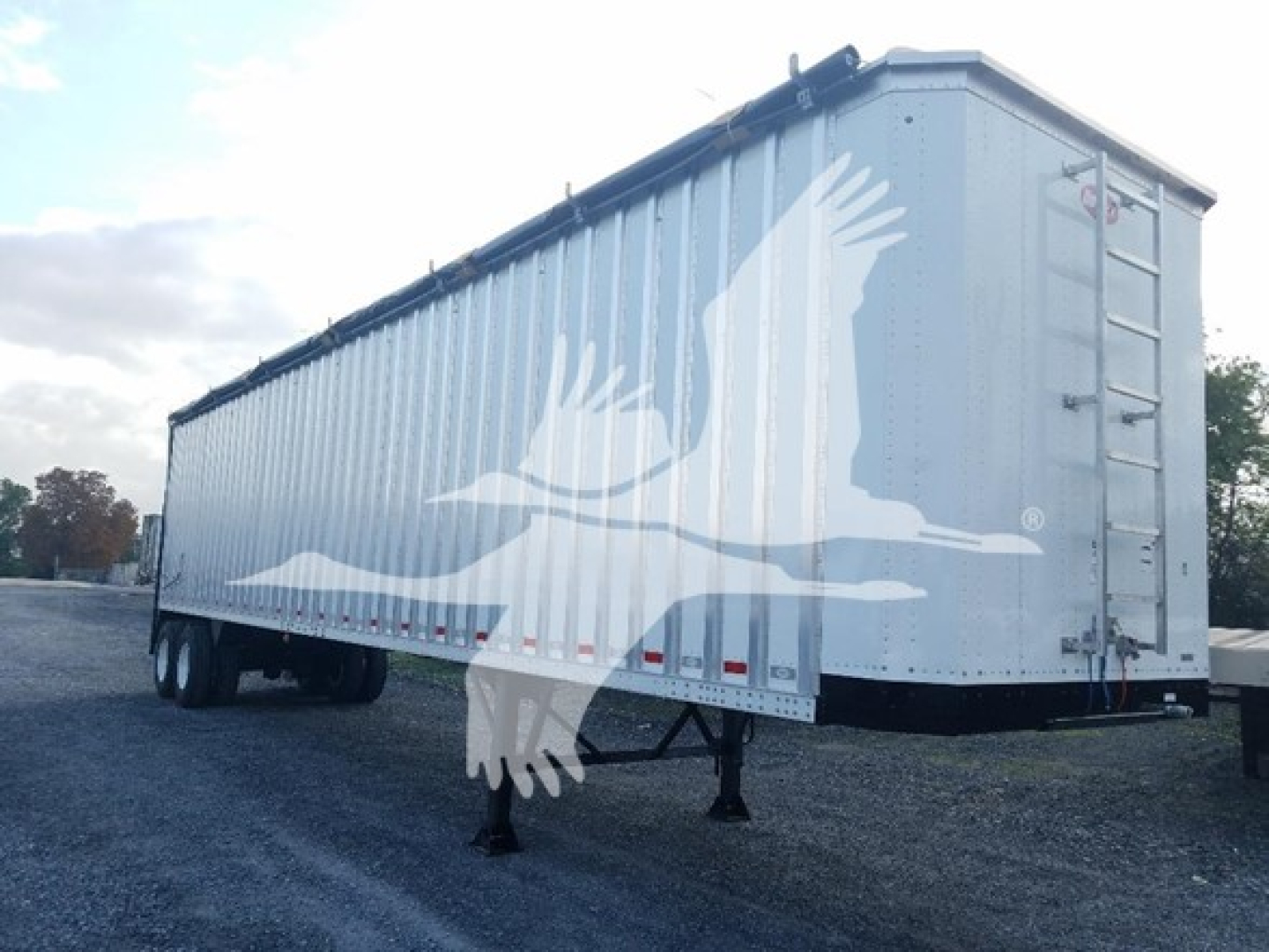 Trailering equipment showing a long silver Dorsey walking floor trailer with a large white bird graphic on the side, rear ladder, and support legs.