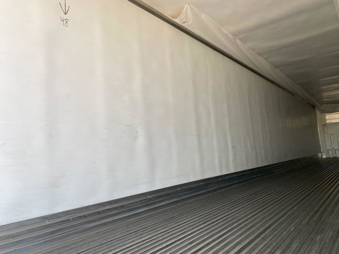 Internal view of a 2021 Utility Reefer trailer cargo area with white insulated walls and ribbed floor; small handwritten markings near roof edge.