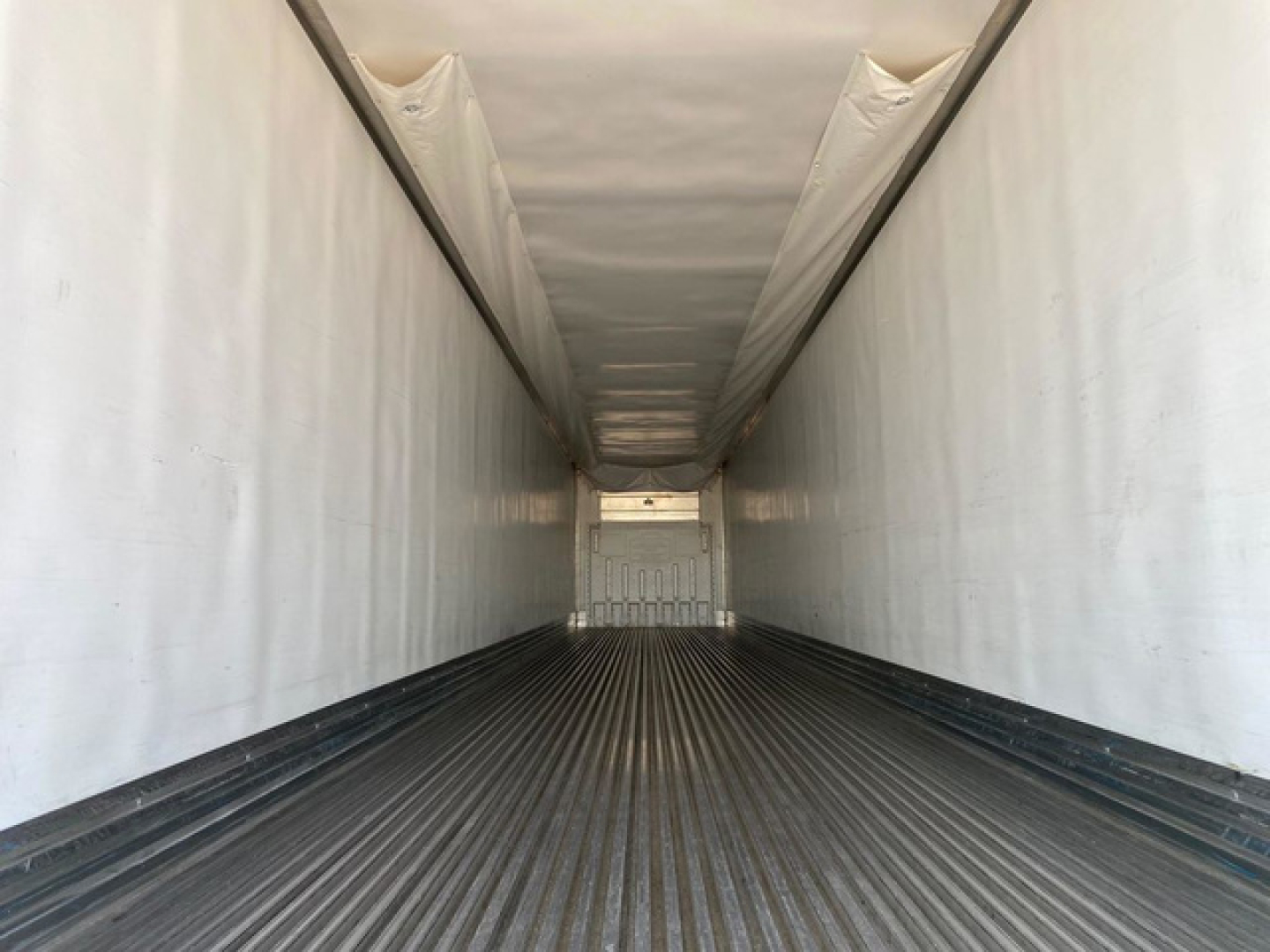 Trailer interior showing empty refrigerated trailer with corrugated floor and smooth white walls, viewed from the rear toward the front.