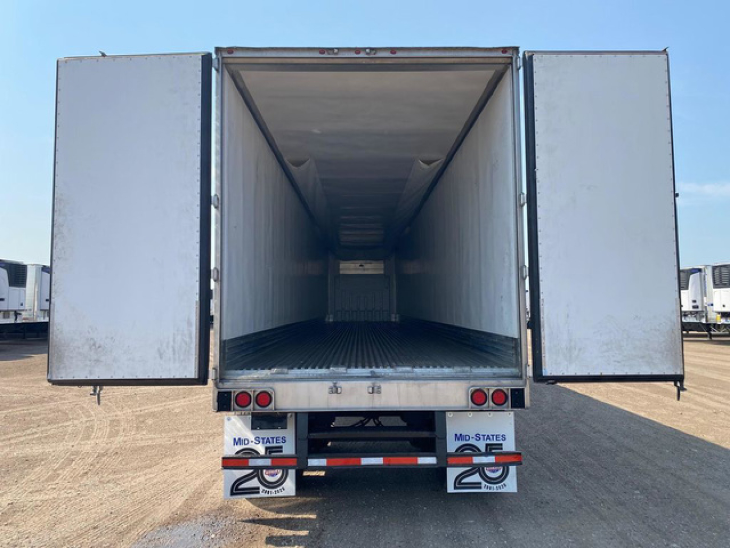 rear view of a refrigerated trailer with wide open doors, empty interior, metal floor, exterior undercarriage with bumper and mud flaps visible
