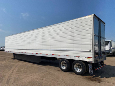 Trailer side view of a refrigerated semi-trailer with metal horizontal siding and dual rear doors. Visible stickers near the rear wheels and frame.