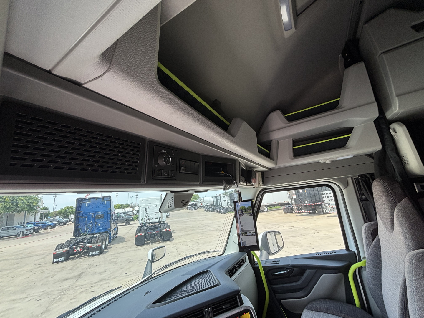 Cab interior of a Volvo VNL truck showing overhead storage and dashboard with a mounted tablet, side window, and driver seat area.