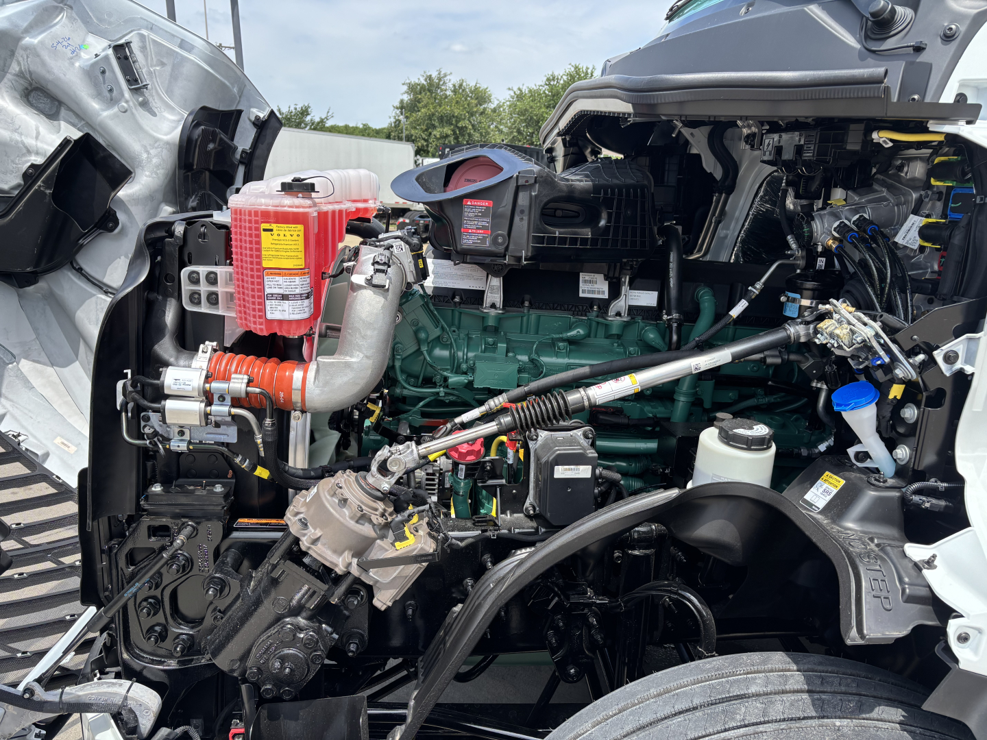 Volvo engine bay showing green Volvo diesel engine with red coolant reservoir and various hoses and components in a truck cab.