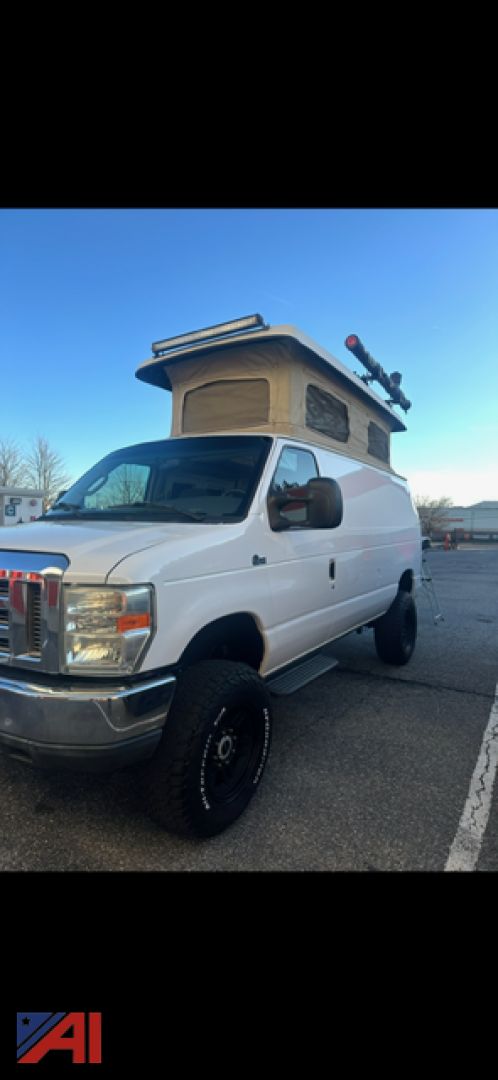 Ford E-Series cargo van with a rooftop pop-up camper and mounted equipment on top, white exterior, in a parking lot.