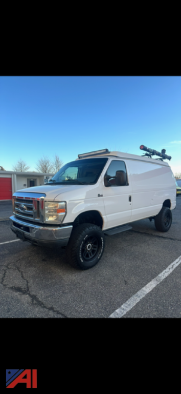 Ford E-350 cargo van with ladder rack in parking lot, white exterior, black wheels, side dual doors visible.