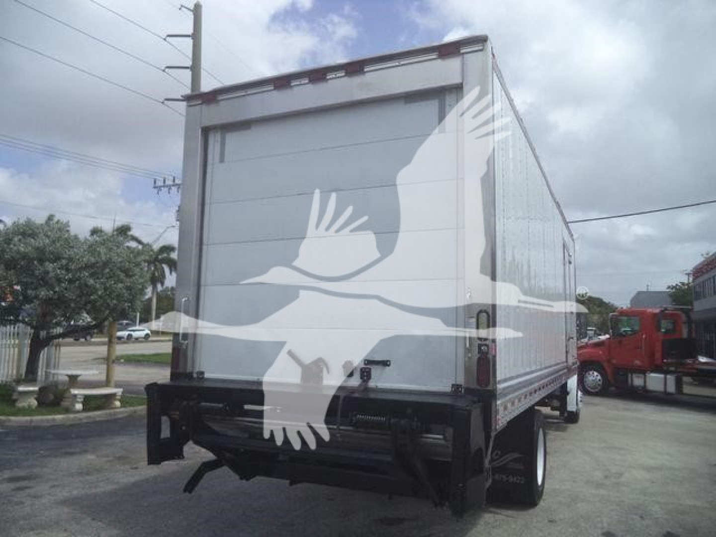 Freightliner M2 106 box truck viewed from rear, with trailer back gate and dual rear tires visible.