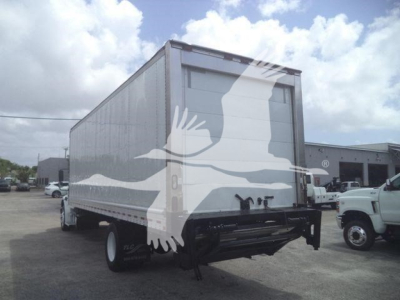 Box truck rear two-thirds view showing Freightliner M2 106 cargo box with roll-up rear door and dual rear wheels.