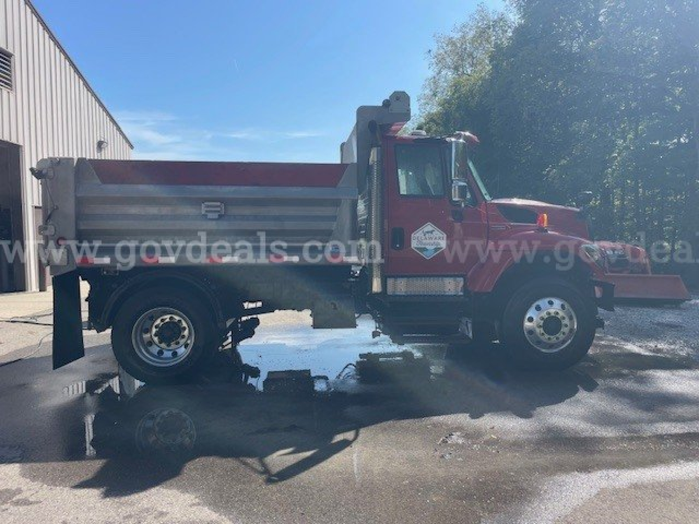 Truck side view of a red International Maxxforce DT 7400 plow truck in service, with a silver dump bed, front grille, and heavy-duty tires.