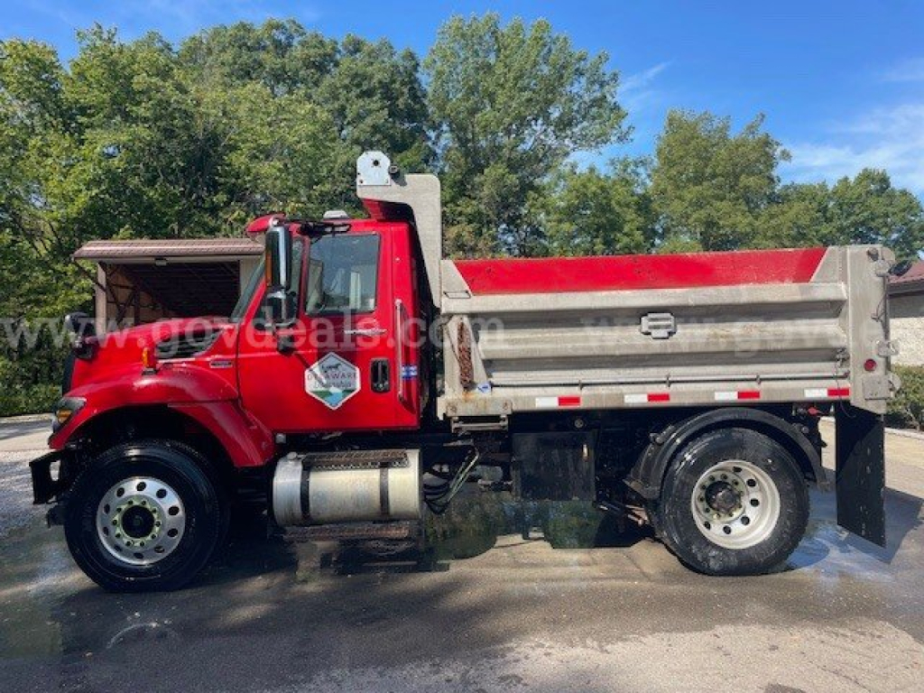 Truck showing a red International dump truck with a silver aluminum bed, plow-ready chassis, DT 7400 series engine badge visible, side view, front cab with International logo.