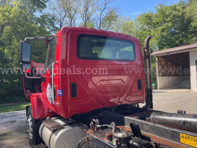 Truck cab rear and chassis of a red 2010 International Maxxforce DT 7400 plow truck showing rear cab windows, fuel tank, and frame.
