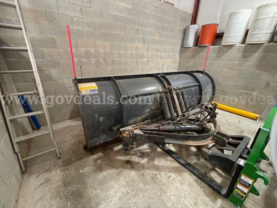 Truck plow equipment mounted in a storage area showing a black Maxxforce DT 7400 plow unit with hydraulic hoses and mounting frame.