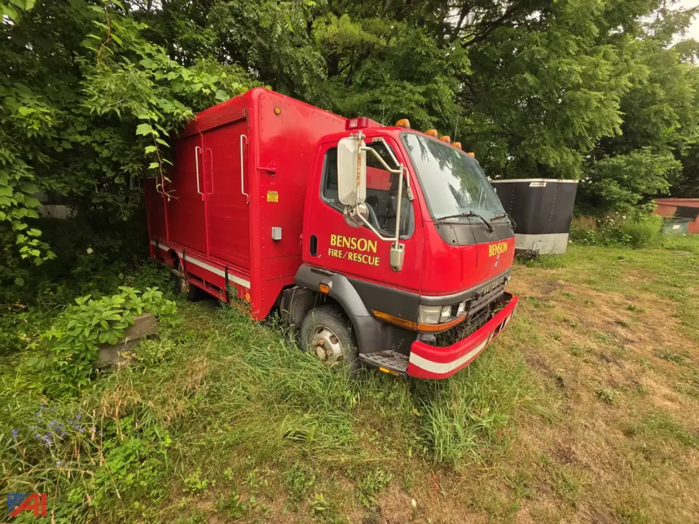 Red Mitsubishi Fuso FH211 rescue truck with multiple compartment doors and Benson Fire/Rescue labeling, front bumper guard, parked on grass.