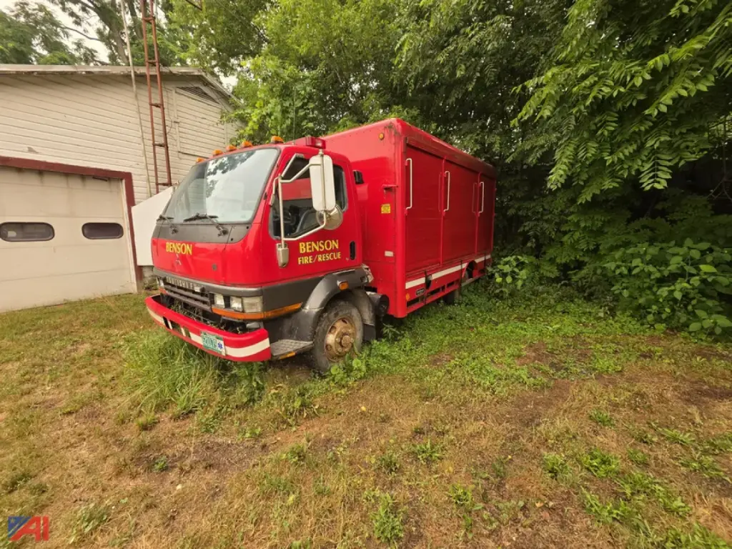 Mitsubishi Fuso FH211 rescue fire truck in red with Benson Fire Rescue markings, cab view, front and left side, parked on grass beside a building.