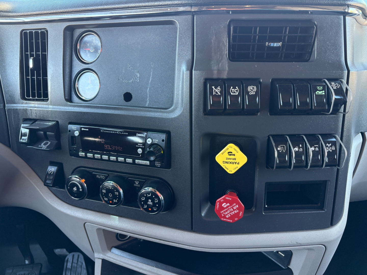 Truck dashboard interior of a 2022 Peterbilt 579 showing instrument cluster, climate controls, radio, switches, and yellow and red warning caps.