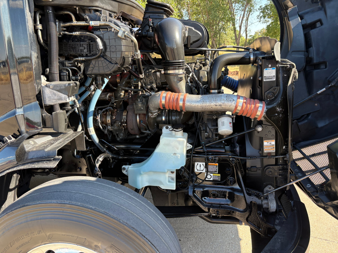 Peterbilt 579 engine bay showing fuel system and turbocharger with orange heat sleeve and light blue coolant reservoir.