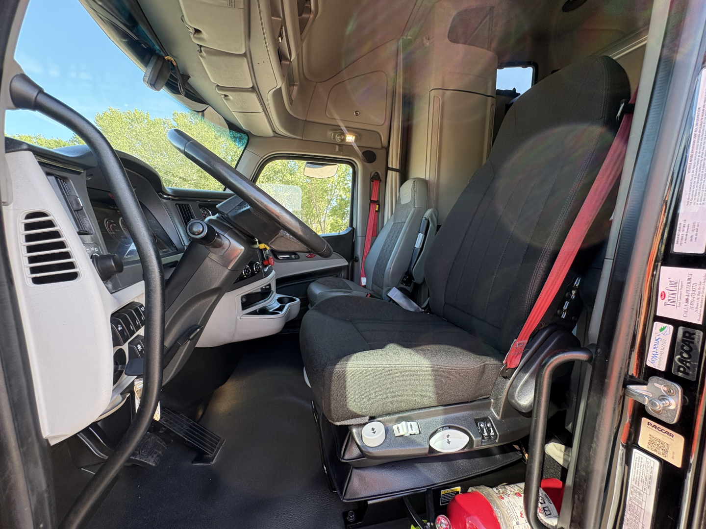 Peterbilt 579 interior cab view showing driver seat with controls, steering wheel, and dashboard from doorway angle.