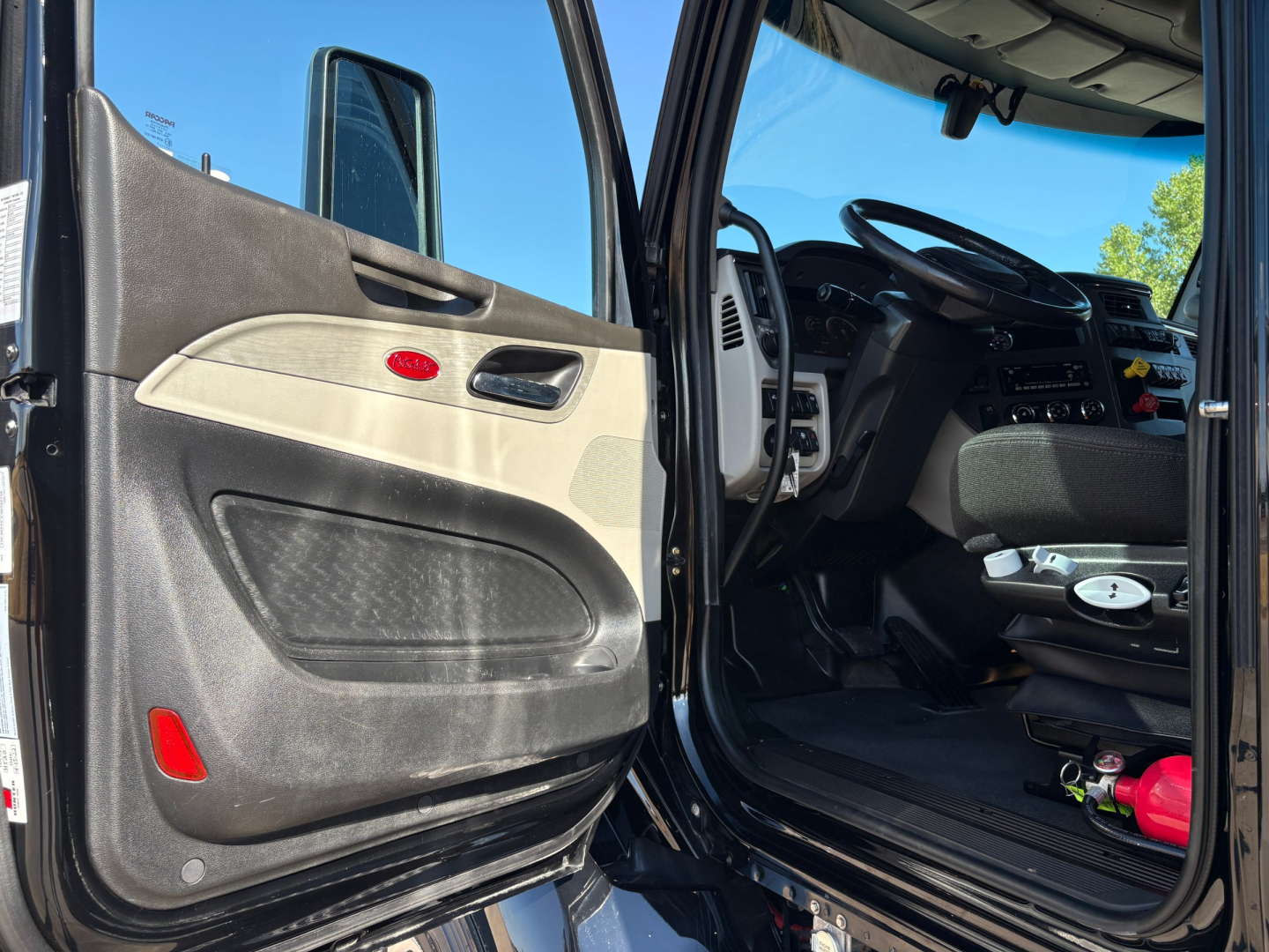 Peterbilt 579 truck interior and driver door open showing the cabin and steering wheel. Visible text on door panel includes red Peterbilt emblem.