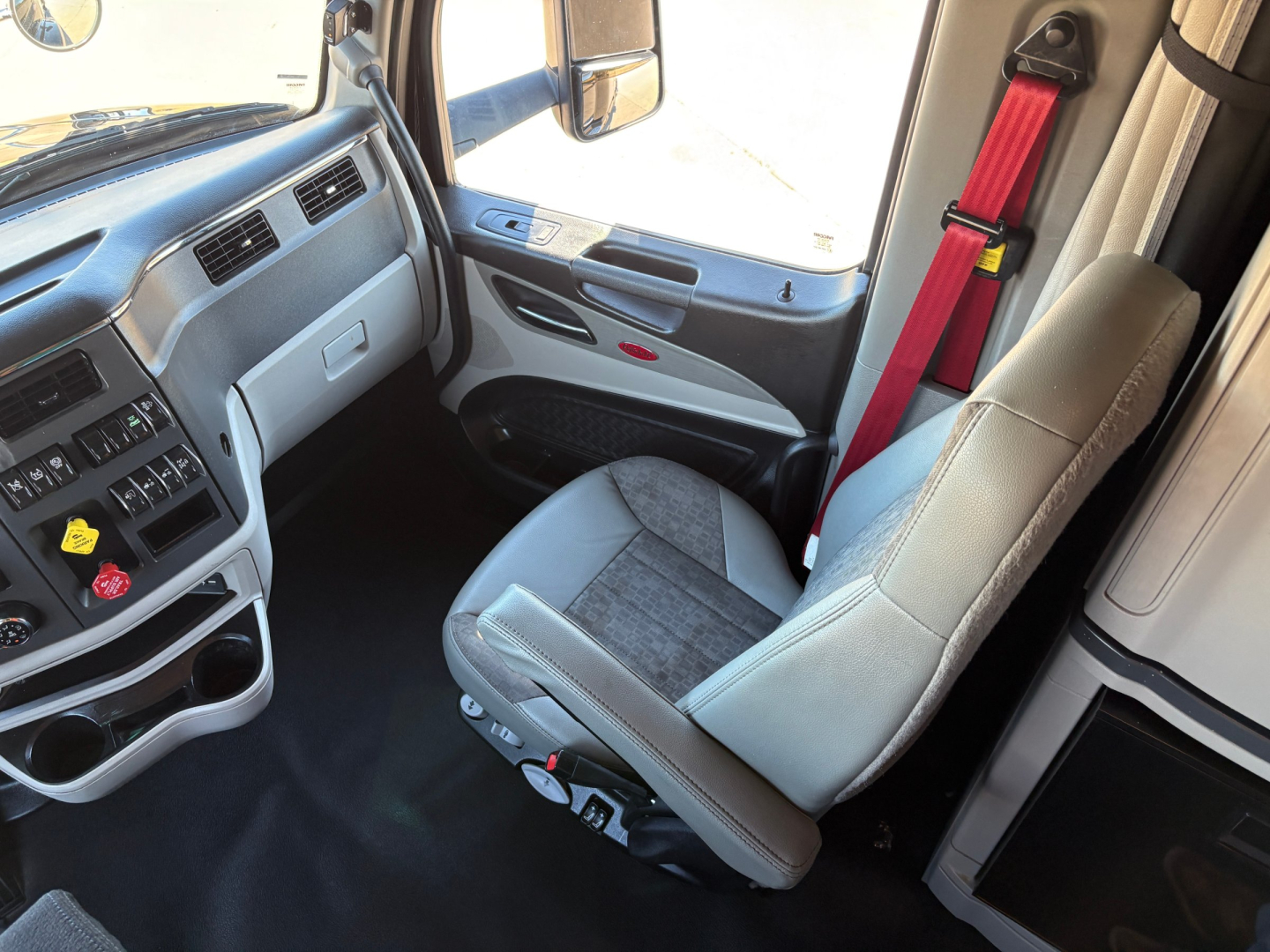 Peterbilt 579 truck interior showing grey fabric driver seat and dashboard with red seat belt near window