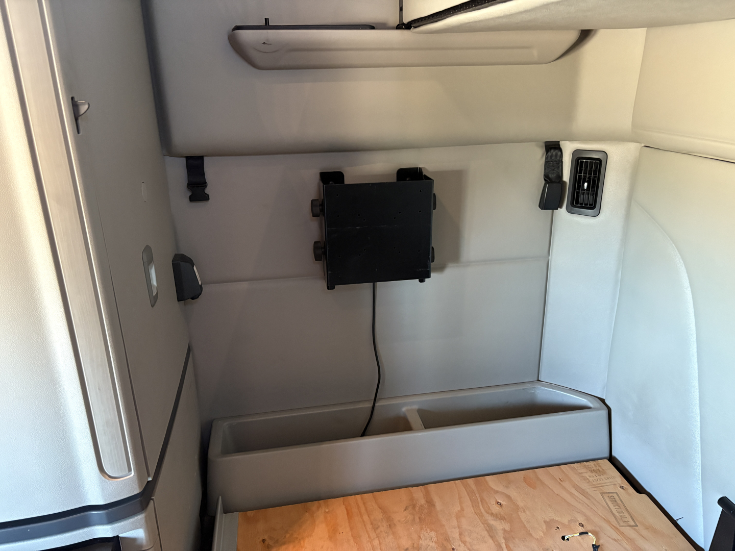 Peterbilt 579 sleeper cab interior panel with mounted black device on wall, vent, wiring, and a small storage tray at the lower wall in the cab.