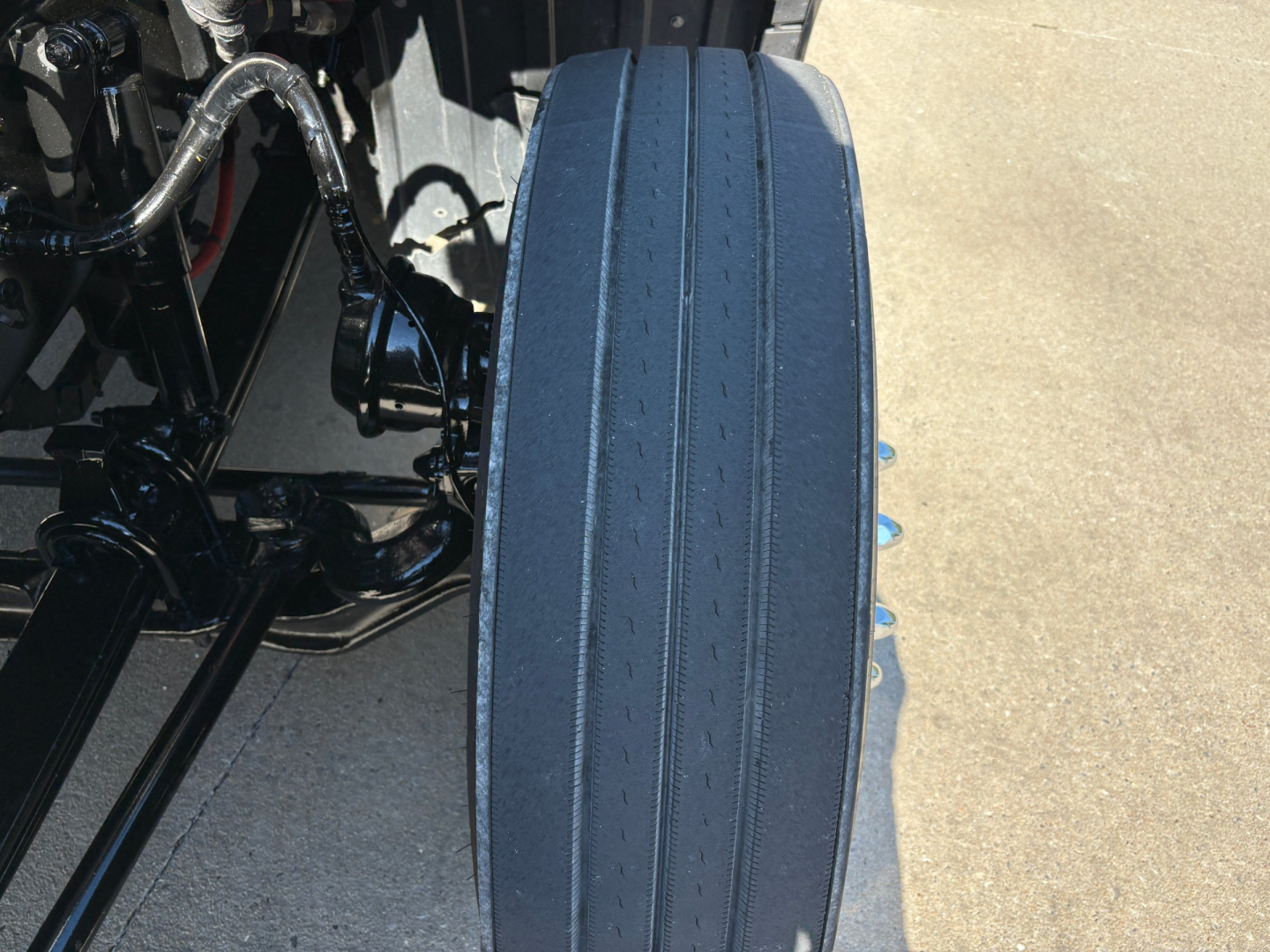 Tire photo on a Peterbilt 579, showing a single black steer/dolly tire with tread grooves and part of undercarriage components.