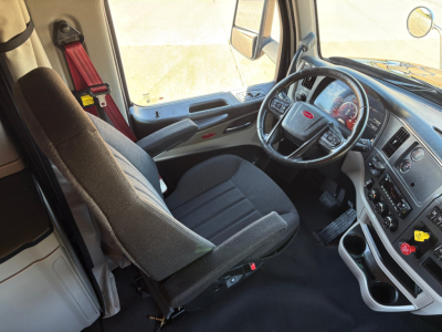 Truck interior seat and dashboard view of a Peterbilt 579 cab, steering wheel with Peterbilt emblem, center console with gauges and controls, driver's seat, window and side mirror.