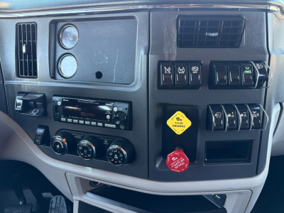 Truck dashboard interior of a 2022 Peterbilt 579 showing instrument cluster, climate controls, radio, switches, and yellow and red warning caps.