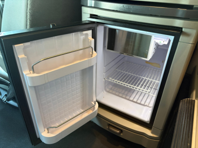 Small fridge/freezer inside a Peterbilt 579 truck cabin with doors open, showing empty freezer compartment and single wire rack shelves.