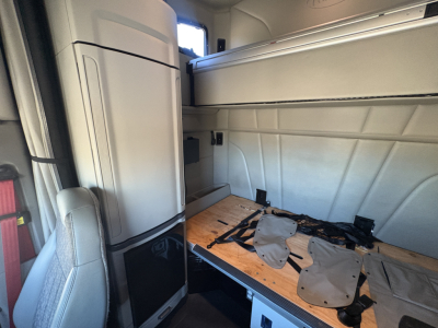 Peterbilt 579 truck cab interior showing sleeper area and storage compartments with a wooden floor panel and seat in view.
