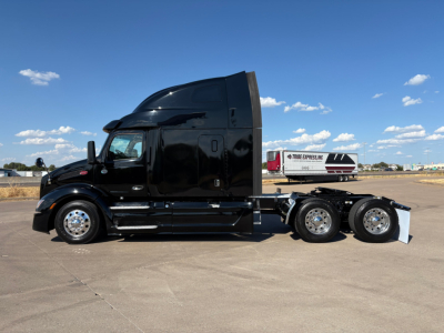 Peterbilt 579 tractor with glossy black exterior, sleeper cab, side view showing dual rear axles and chrome wheels.