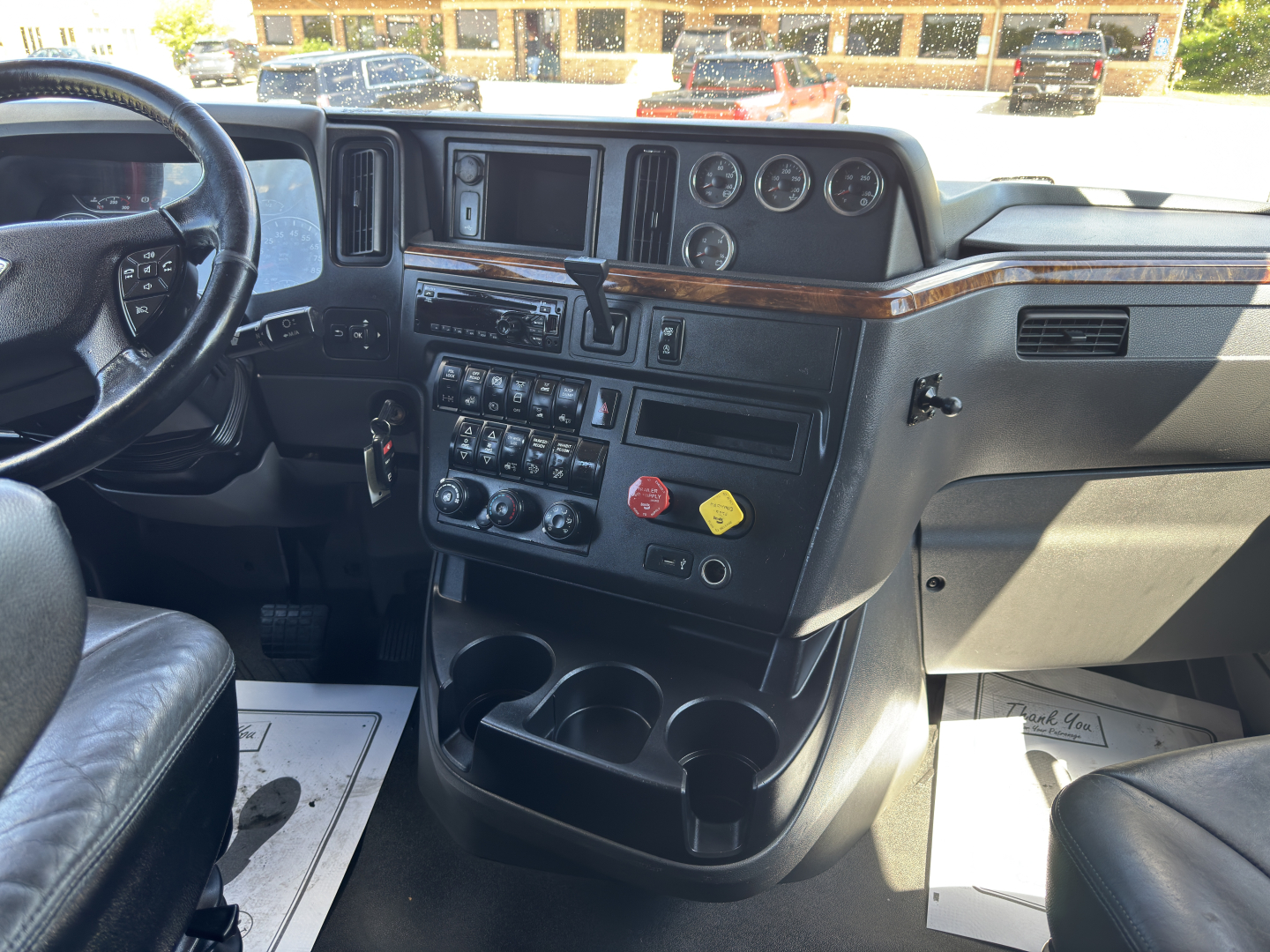 Truck cab interior showing dashboard with multiple gauges, steering wheel, control panel, and cup holders in a 2019 International LT625 truck.