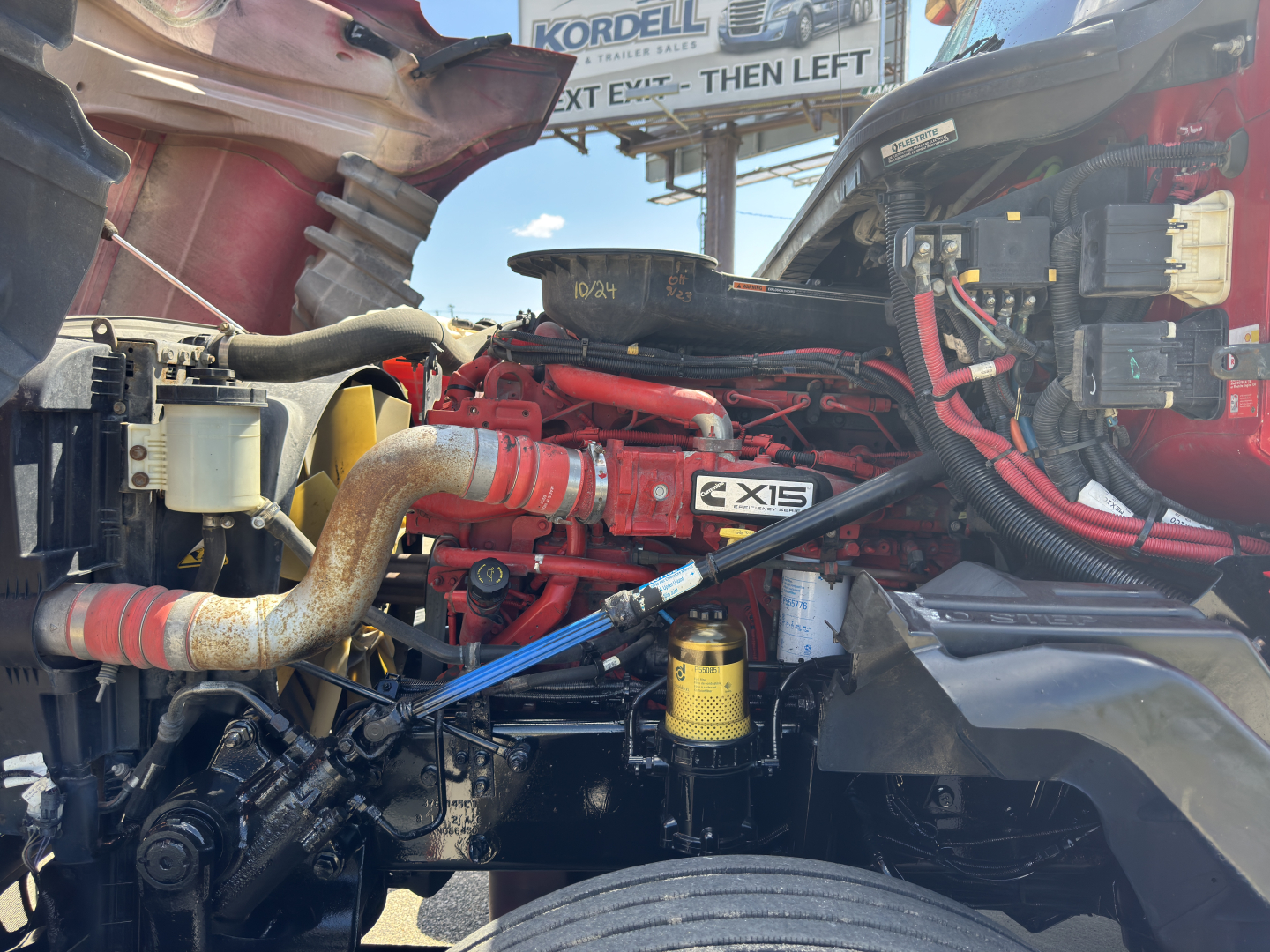 Engine bay of a 2019 International LT625 truck showing red engine components, hoses, and a yellow filter. Visible labels include X15 badge and various hoses and wiring.